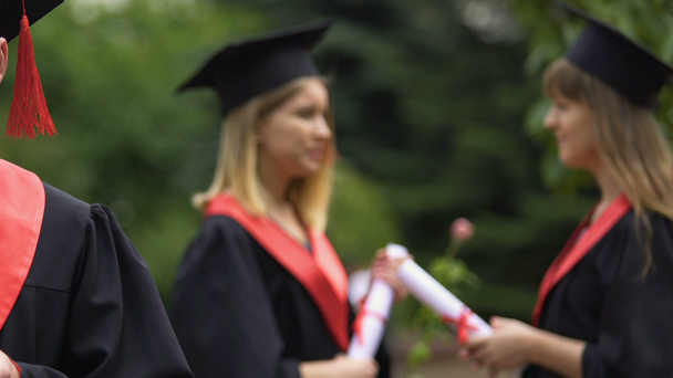 Деактивовані жінки-випускниці в академічній сукні розмовляють, тримаючи дипломи в руках
 - Кадри, відео