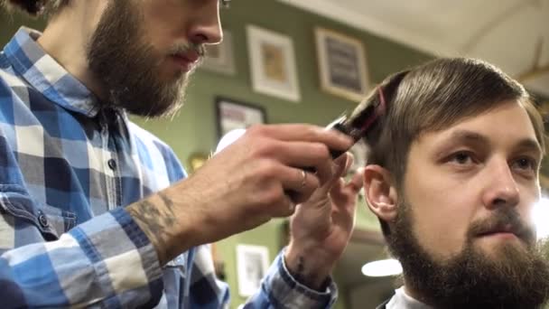 Portréja egy szakállas fodrász, így a fodrász ügyfele, fésű és a trimmer figyelmesen. 4k - Felvétel, videó