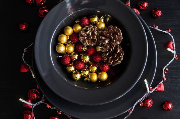 Christmas Decorations in the black plate on the dark background .Red,golden balls and cones inside and christmas light around. - Foto, Imagen