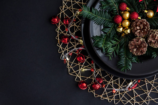 Decorações de Natal na placa preta no fundo escuro com alguns ramos de abeto. Vermelho, bolas de ouro e cones dentro e luz de Natal ao redor
. - Foto, Imagem