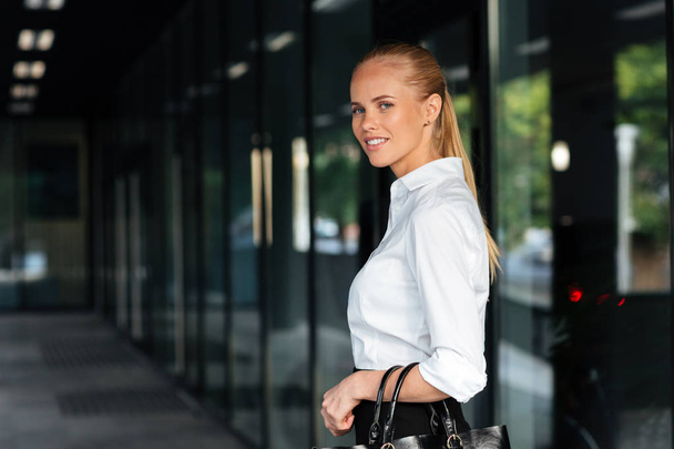 Young smiling businesswoman standing and holing handbag - Zdjęcie, obraz