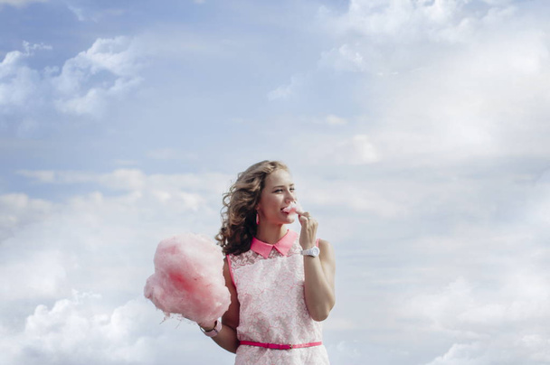 beautiful young blonde girl eats cotton candy in the summer on a blue sky background - Zdjęcie, obraz