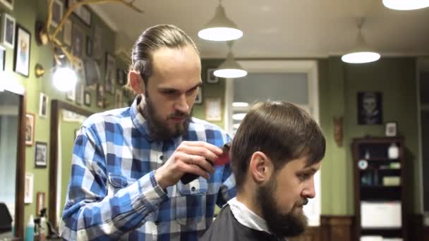 Concentrated Barber cutting hair with electric razor in barber shop - Filmagem, Vídeo