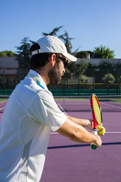 Jugador de tenis profesional está haciendo una patada de tenis en una pista de tenis en una soleada mañana de verano
. - Foto, imagen