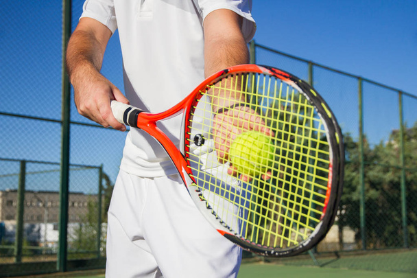 Close up photo of a racket and a tennis ball. Both are held by a professional tennis player with his hands. - Photo, Image