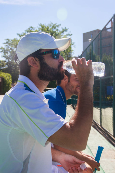 Two professional players hydrating after a hard game of tennis. They are sitting resting for the game. - Fotó, kép