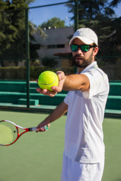 Tennisprofi, bärtiger junger Mann bietet Tennisball zum Spielen an.  - Foto, Bild