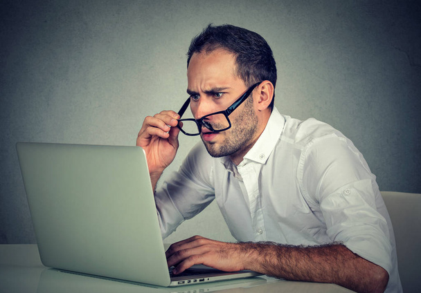 silmälasipäinen mies, jolla on näköongelmia kannettavan tietokoneen ohjelmiston kanssa
  - Valokuva, kuva