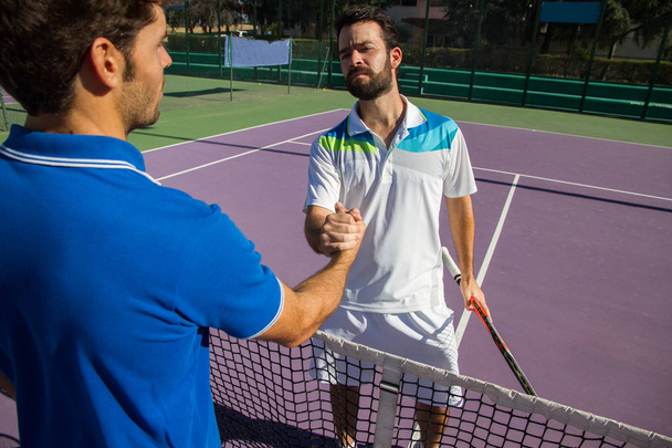 Двоє чоловіків, професійні тенісисти тремтять руками до і після тенісного матчу. Одна з них має обличчя гніву
. - Фото, зображення