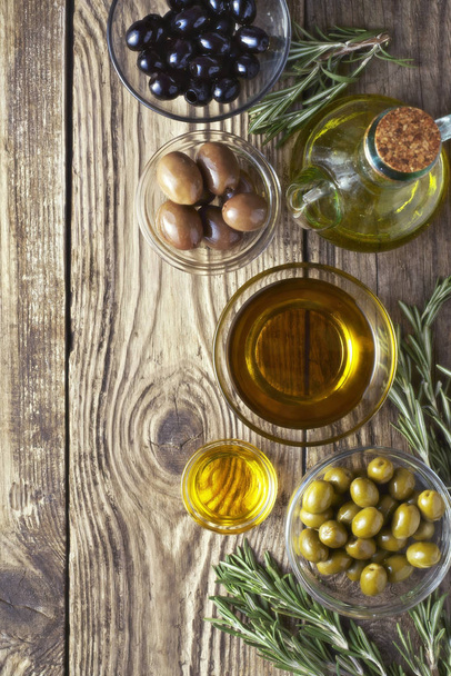Olives with olive oil and rosemary on the wooden table - Fotoğraf, Görsel