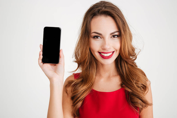 Smiling woman in red dress showing blank smartphone screen - Valokuva, kuva