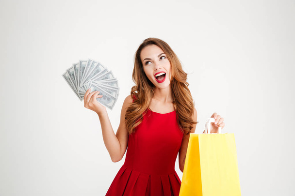 Happy woman in red dress holding shopping bag and money - Foto, afbeelding