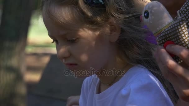 ένα μικρό κορίτσι που κάθεται σε ένα παγκάκι στο πάρκο της πόλης - Πλάνα, βίντεο