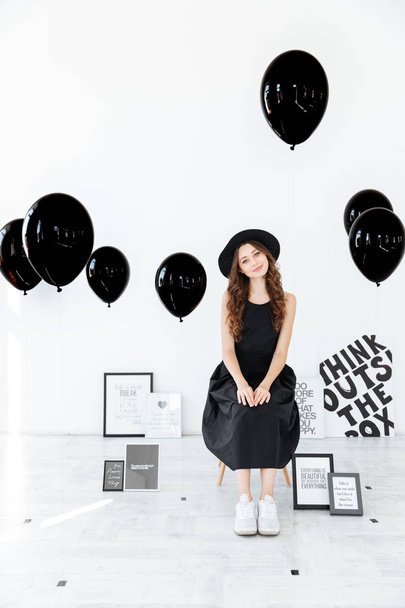 Smiling woman sitting over white background with posters and balloons - Foto, imagen