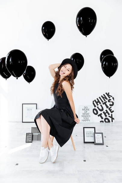 Playful young woman with posters and black balloons showing tongue - Foto, Imagem