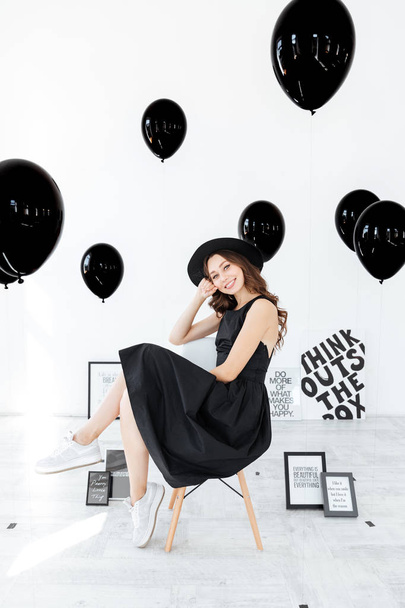 Happy beautiful young woman sitting with posters and black balloons - Φωτογραφία, εικόνα