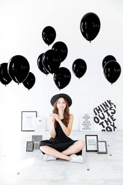 Happy woman sitting with legs crossed and holding black balloons - Φωτογραφία, εικόνα