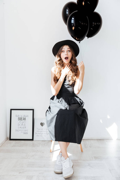 Surprised lovely young woman holding black balloons - Fotó, kép