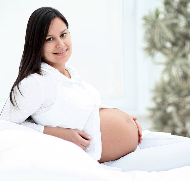 Pregnant woman lying on the bed, smiling and looking into the camera - Φωτογραφία, εικόνα