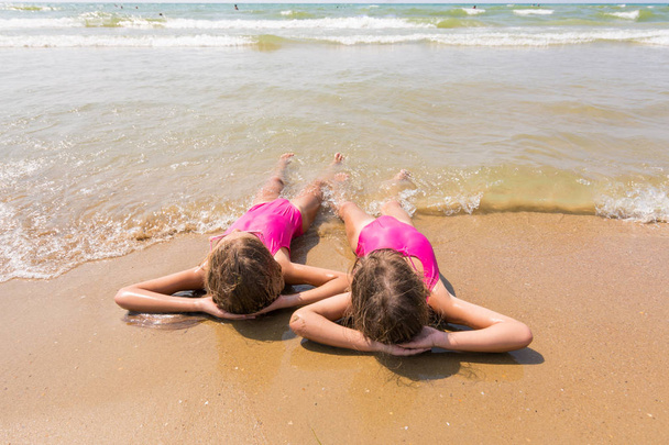 Two girls lie on your back on the sandy beach and looking at sea - Photo, Image
