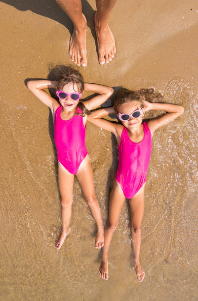 Dvě dívky ležet na zádech na příboj moře, písčité pláže, existuje celá řada dospělých lidská noha - Fotografie, Obrázek