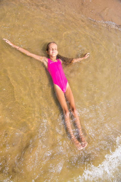 Siete años chica se acuesta boca arriba en el agua en la playa de arena
 - Foto, Imagen