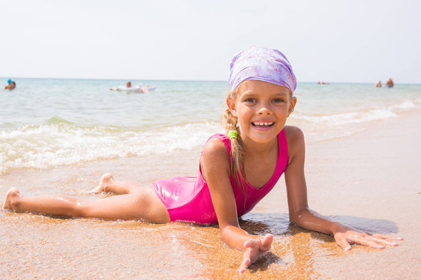 Šťastná dívka ležící na písku u vody na pláži a šťastně se usmívala vypadá do rámu - Fotografie, Obrázek