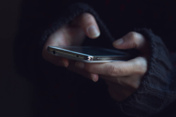Primer plano de la mujer en manos suéter oscuro sosteniendo un teléfono
  - Foto, imagen