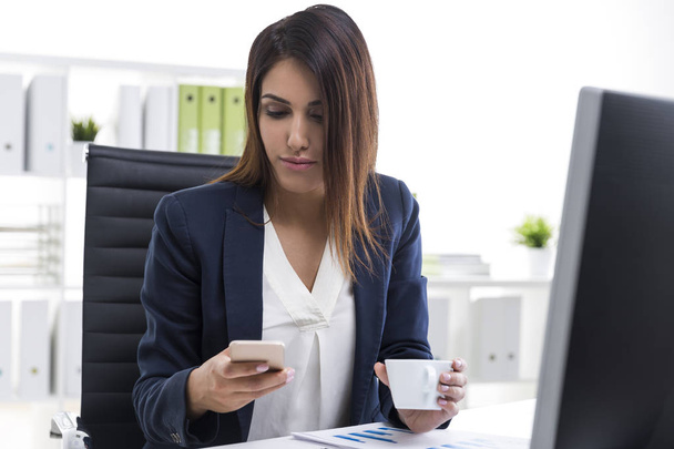 Mujer de negocios con su teléfono celular y una taza de café
 - Foto, Imagen