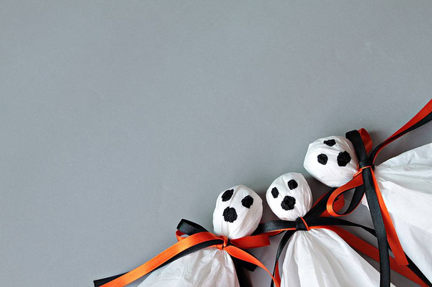 Three halloween ghosts DIY made from white tissue paper, black and orange ribbon on gray background - 写真・画像