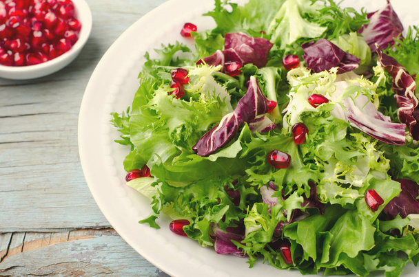 grüner Salat mit Spinat, Frisee, Rucola, Radicchio und Granatapfelkernen auf blauem Holzgrund - Foto, Bild