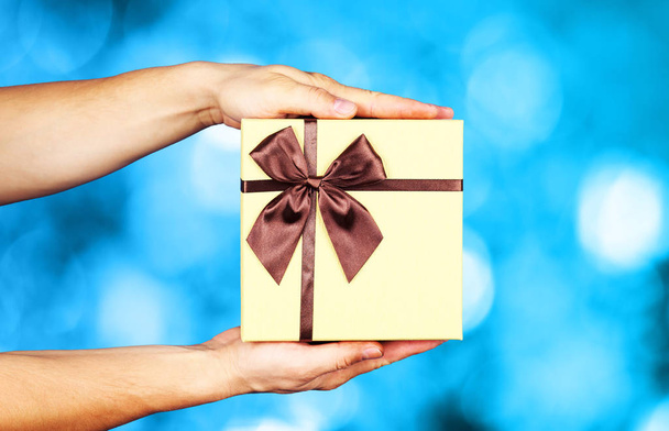 Menselijke hand met bruin lint gewikkeld vakantie verrassing cadeau  - Foto, afbeelding
