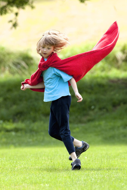 Poika juoksentelee ympäriinsä punaisessa pyyhkeessä supersankarin viittana
 - Valokuva, kuva