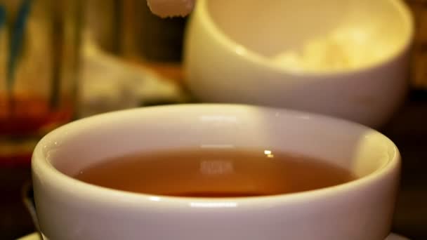 Přidání kusový cukr s kleštěmi na černý čaj v poháru - Záběry, video