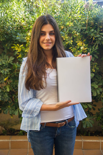 Chica emprendedora bastante blanca con ojos azules sosteniendo un cuaderno en blanco con sus manos donde se puede adjuntar un texto, un contorno o una imagen
. - Foto, imagen