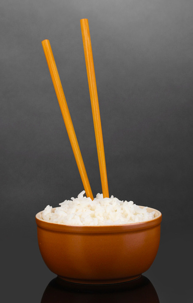 Bowl of rice and chopsticks on grey background - Foto, afbeelding