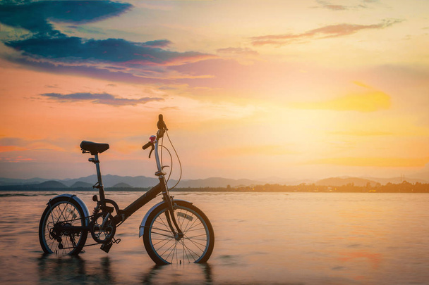 De fiets van het silhouet op het strand bij zonsondergang. Vintage Toon  - Foto, afbeelding