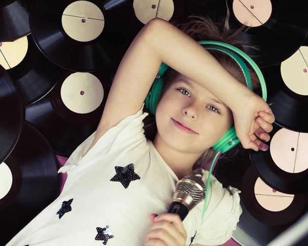 Beautiful girl lying next to vinyl records holding a microphone and listening music on headphones. - Foto, Bild