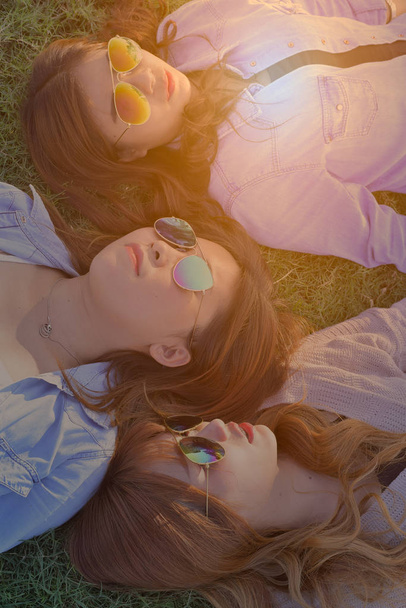 Tres mujeres con gafas de sol, tumbadas sobre hierba verde
. - Foto, imagen