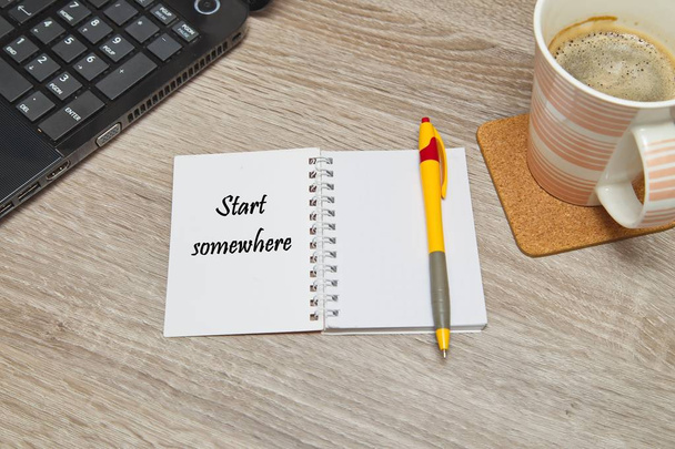 Open notebook with Text "Start Somewhere" and a cup of coffee on wooden background.  Top down view - Foto, imagen