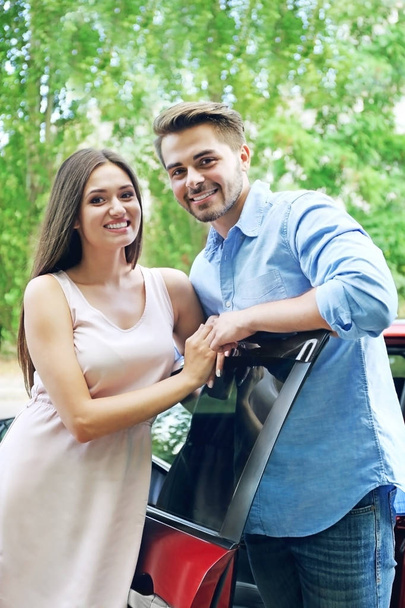 Beautiful young couple standing near red car - Foto, imagen