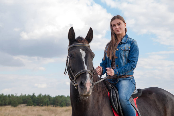 Portrait young girl in a denim suit on a dark horse. - Photo, Image