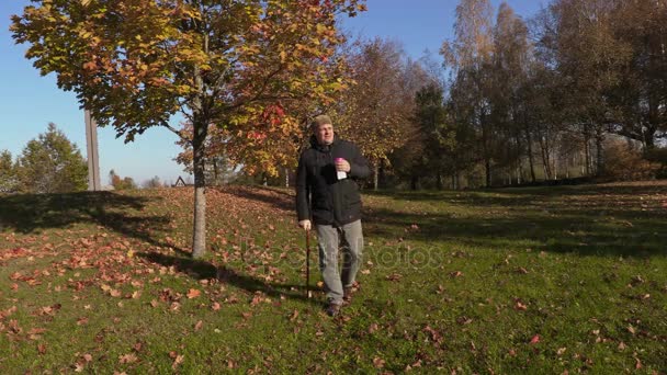 Mies, jolla on keppi, juo kahvia ja kävelee puistossa
  - Materiaali, video