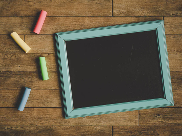 Chalkboard and colorful chalks over wooden table. 3D illustration - Foto, Imagen