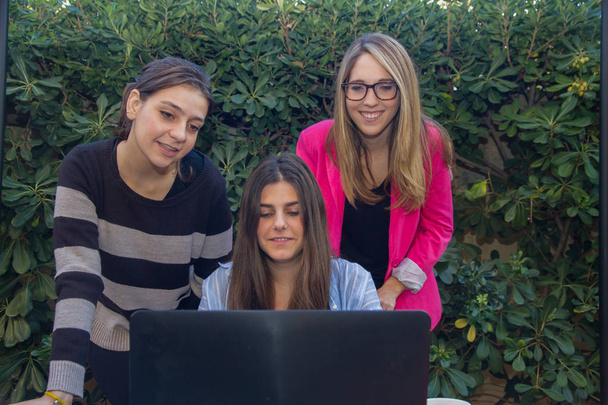 Jóvenes emprendedores trabajando con un portátil. Son tres hermosas chicas caucásicas que están creando su compañía. Trabajan en la terraza de su casa
. - Foto, imagen