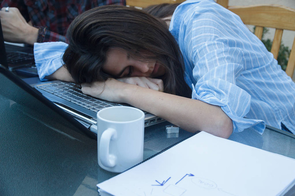 Çok çalışmaktan yorgun genç girişimci kız, o masada üstünde tepe-in belgili tanımlık laptop uykuya dalar. - Fotoğraf, Görsel