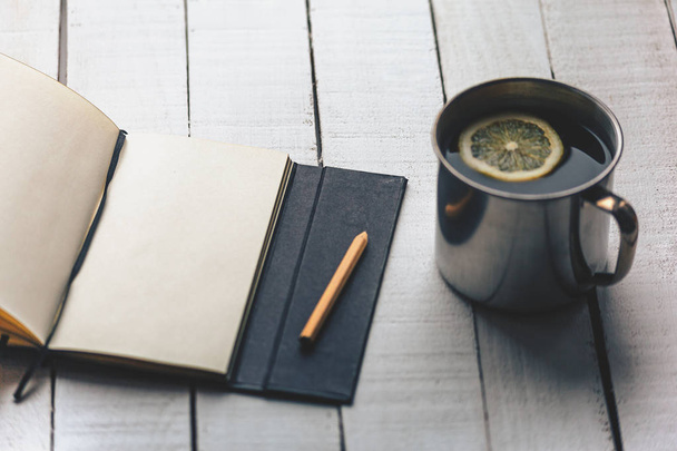 Filiżanka herbaty z cytryną, notebook, ołówek na tle biały prosty drewniany stół - Zdjęcie, obraz