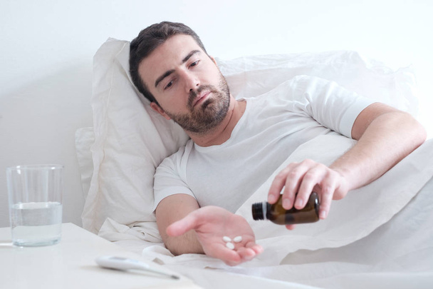 Mann nimmt Medikamententabletten im Bett liegend - Foto, Bild