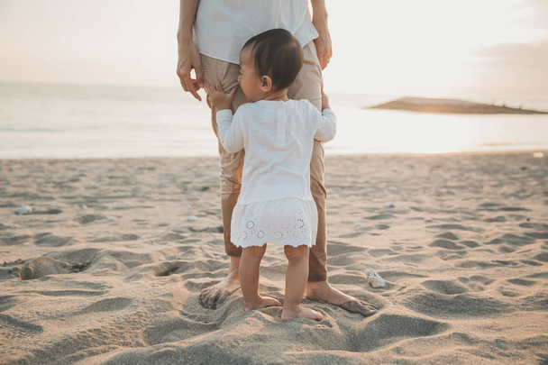 girl holding on mum's leg while standing on the beach - Photo, Image