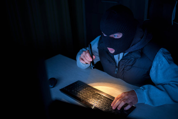 マスクやパーカーの暗い部屋でノート パソコンを使用しての犯罪者 ロイヤリティフリー写真 画像素材
